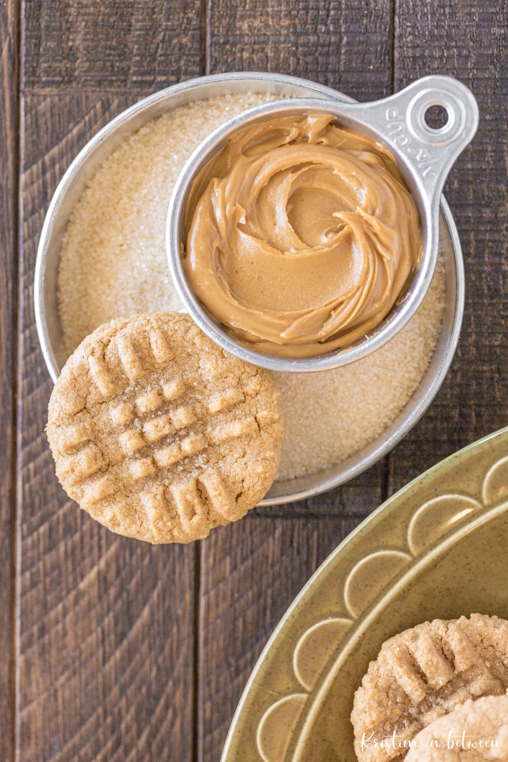 One cookie sitting in a bowl of sugar with a bowl of peanut butter next to it.