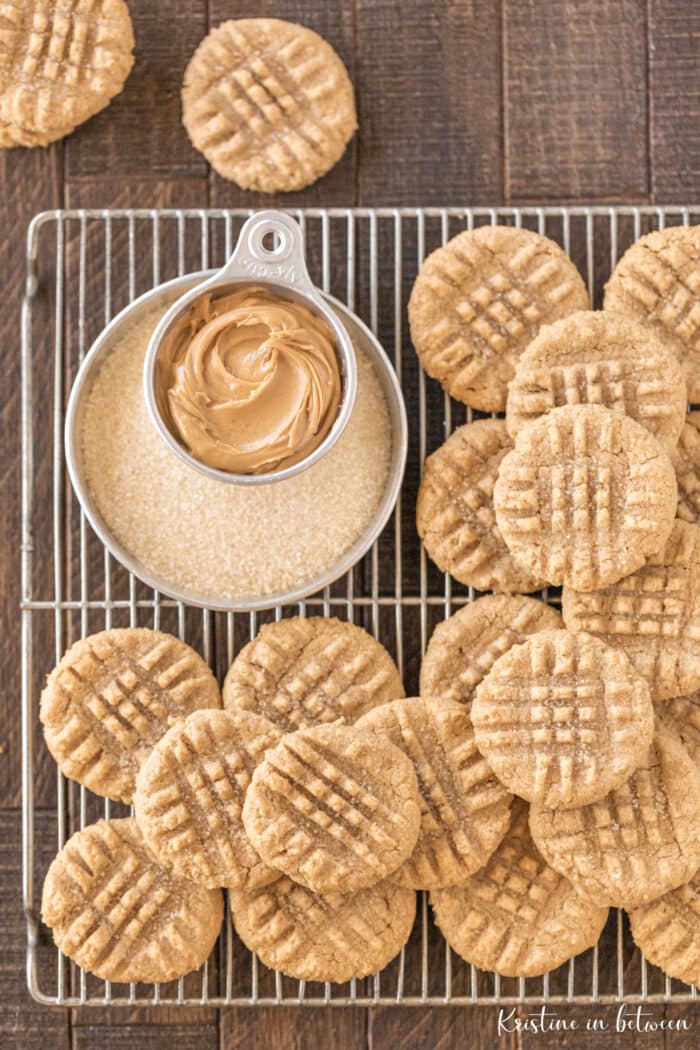 Cookies piled up on a baking rack with a small bowl of peanut butter next to them.