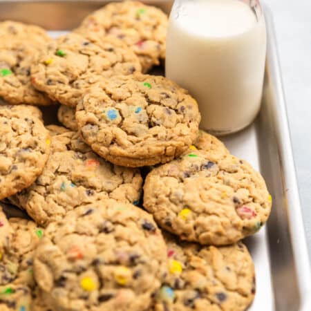 A whole tray of monster cookies sitting with a glass of milk and an orange napkin.