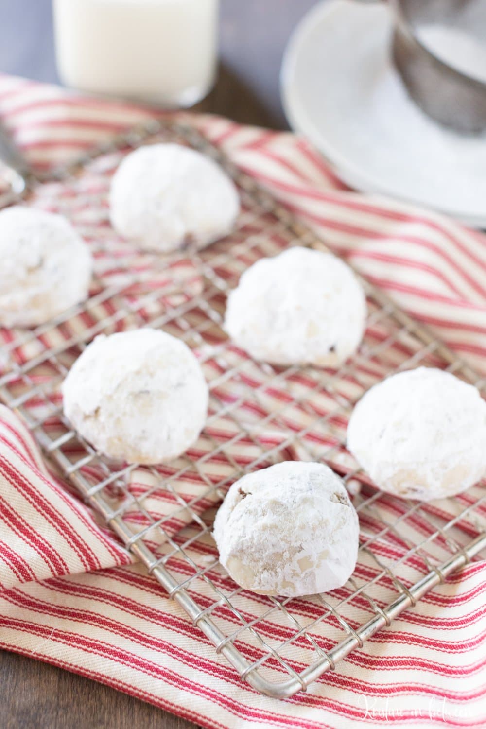 Cookies covered in powdered sugar sitting on a wire rack with a red and white striped napkin underneath them.