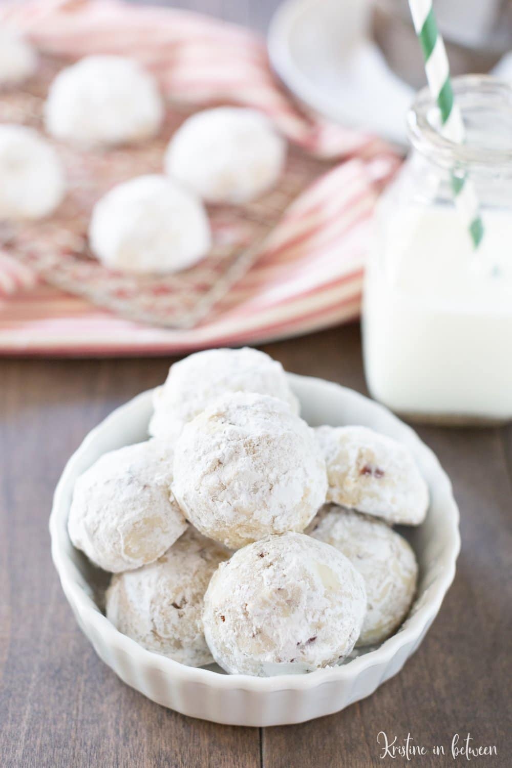 Pecan snowball cookies sitting in a bowl with a jar of milk sitting next to them.