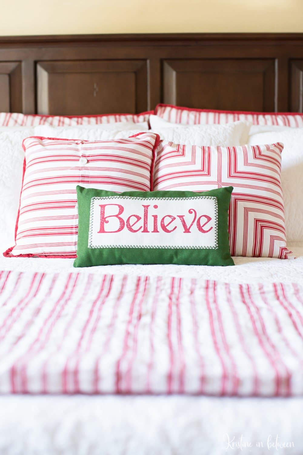 A bed with red and white striped bedding and a green accent pillow that says Believe.