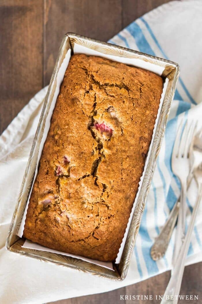 A loaf of strawberry banana bread in an antique loaf pan with two forks sitting next to it.