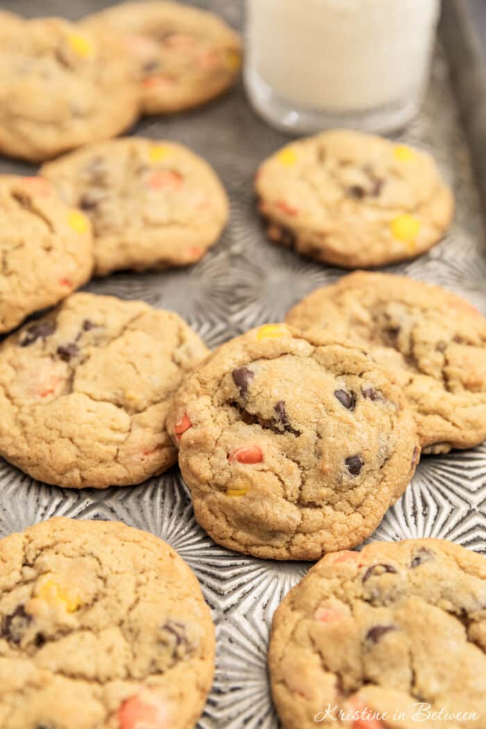 Reese's Pieces cookies laying on an antique baking sheet with a small glass of milk.