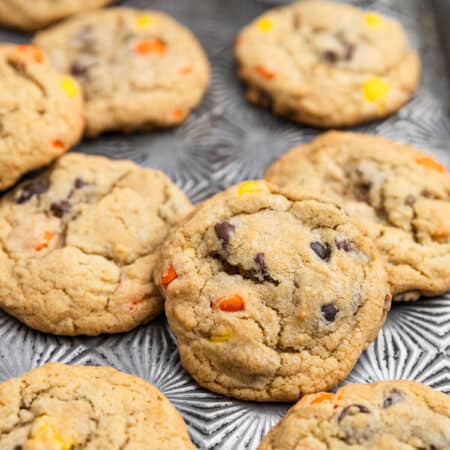 Reese's Pieces cookies laying on an antique baking sheet with a small glass of milk.