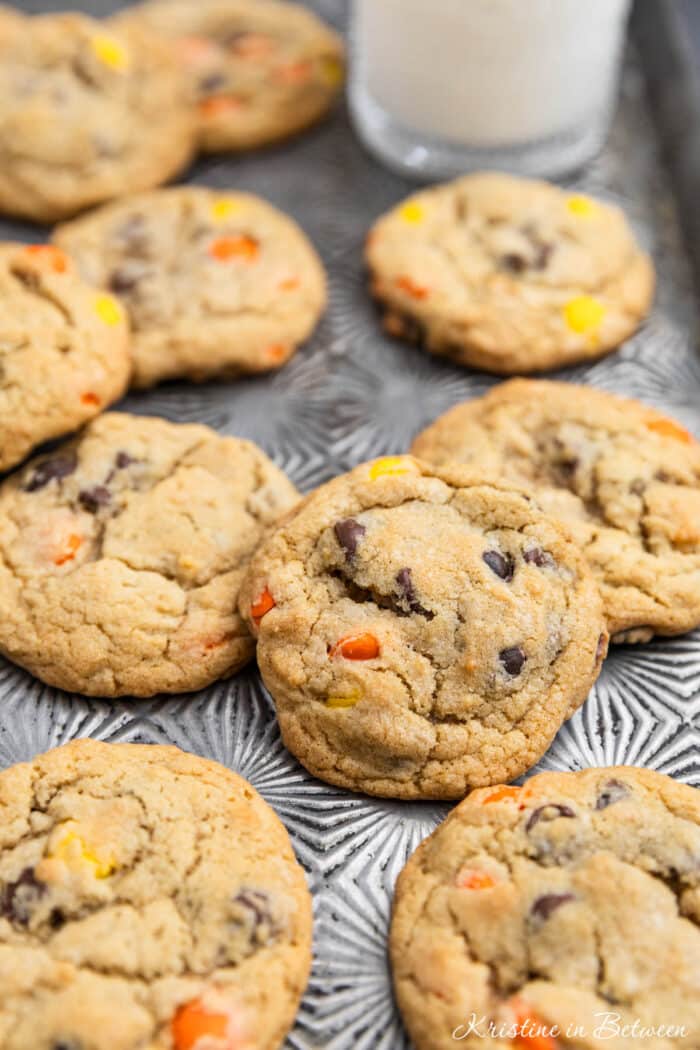 Reese's Pieces cookies laying on an antique baking sheet with a small glass of milk.