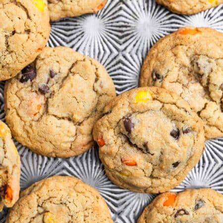 Reese's Pieces cookies laying on an antique baking sheet with a small glass of milk.