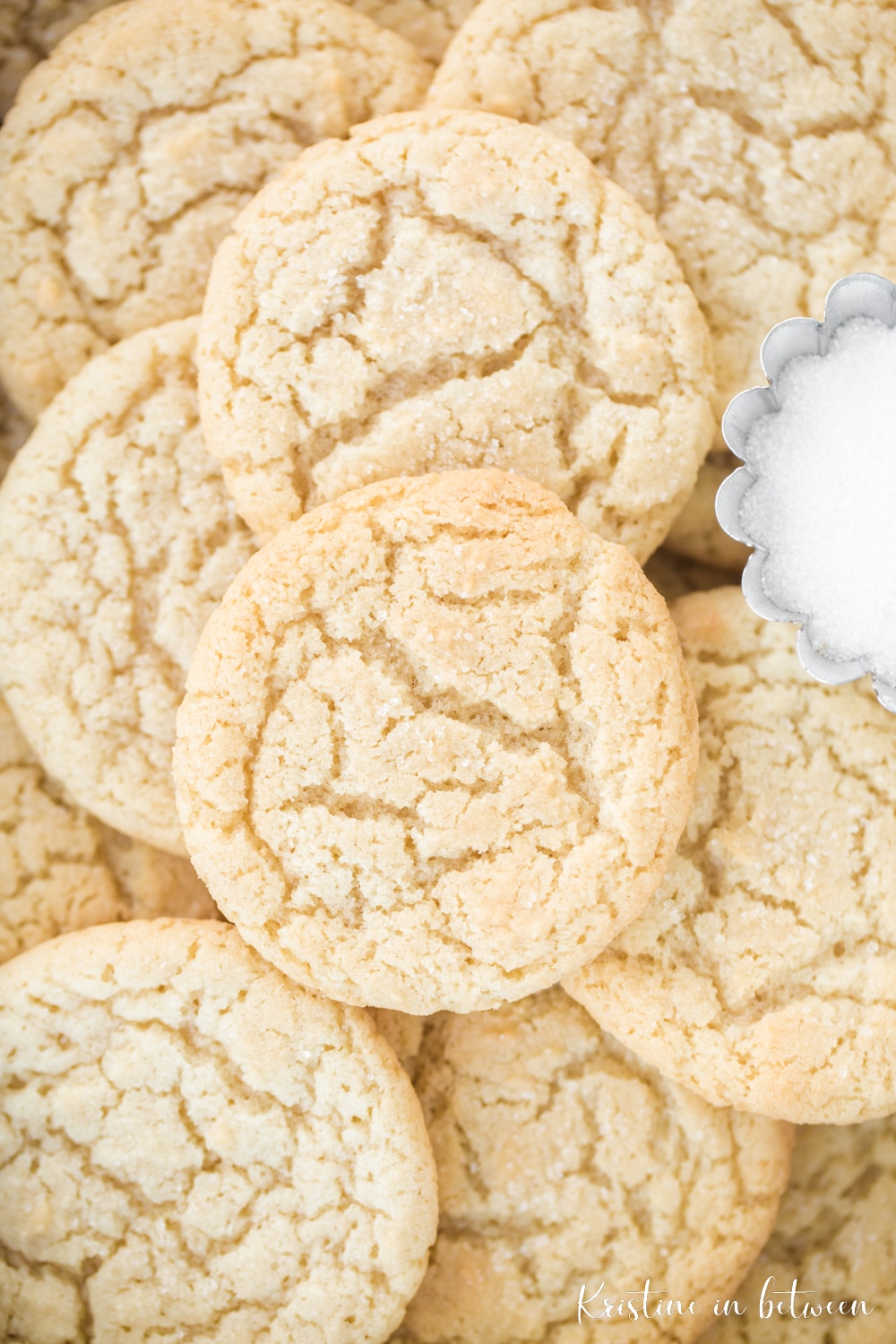 A stack of sugar cookies with a bowl of sugar sitting next to them.