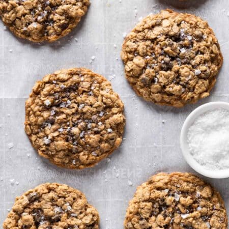 Oatmeal dark chocolate chunk cookies sitting on an antique baking tray with a small bowl of salt next to them.