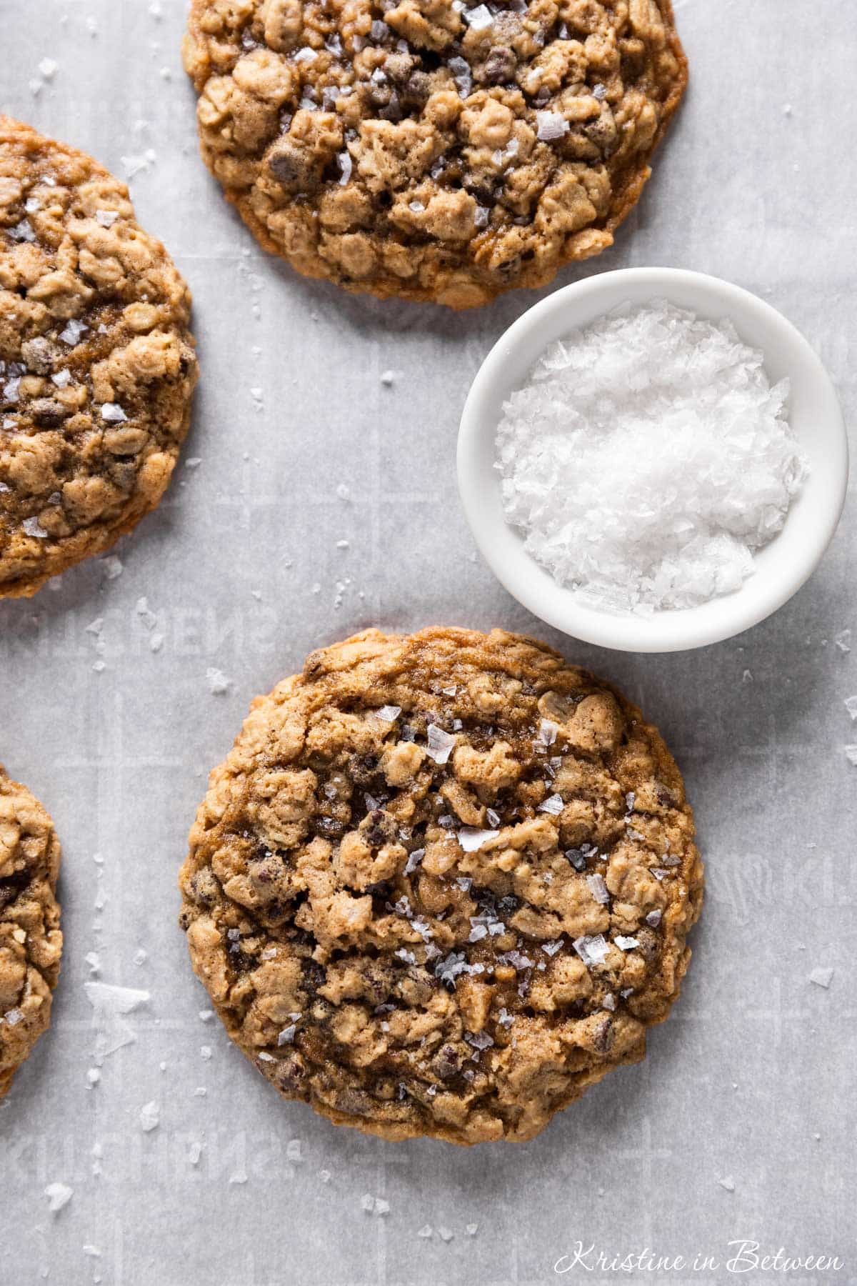 Oatmeal dark chocolate chunk cookies sitting on an antique baking tray with a small bowl of salt next to them.
