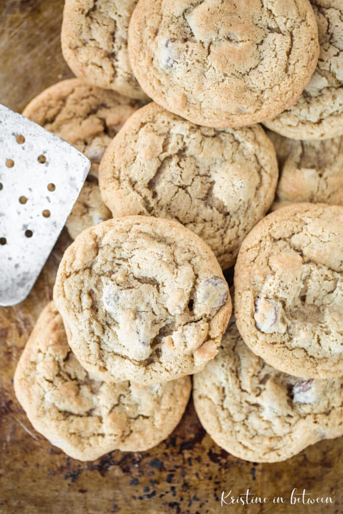 Chocolate chip cookies sitting on a baking sheet with an antique spatula.
