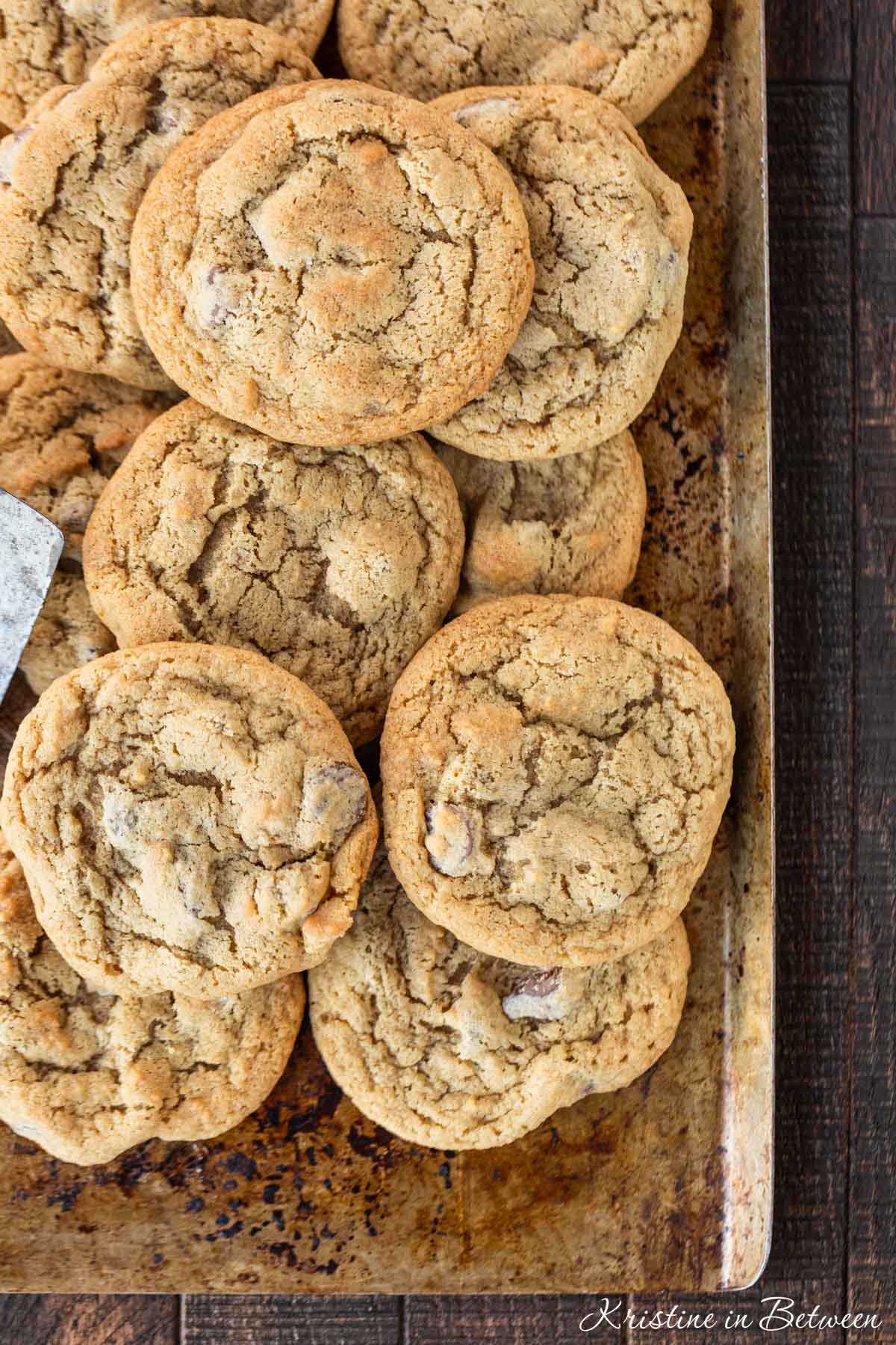 A bunch of cookies laying on an old baking sheet with a spatula.
