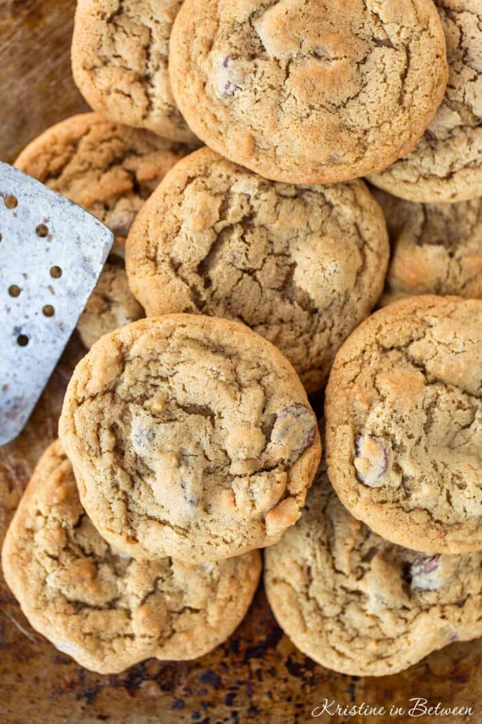 A bunch of cookies laying on an old baking sheet with a spatula.