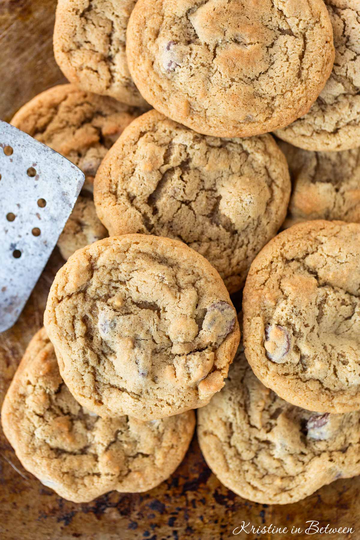 A bunch of cookies laying on an old baking sheet with a spatula.