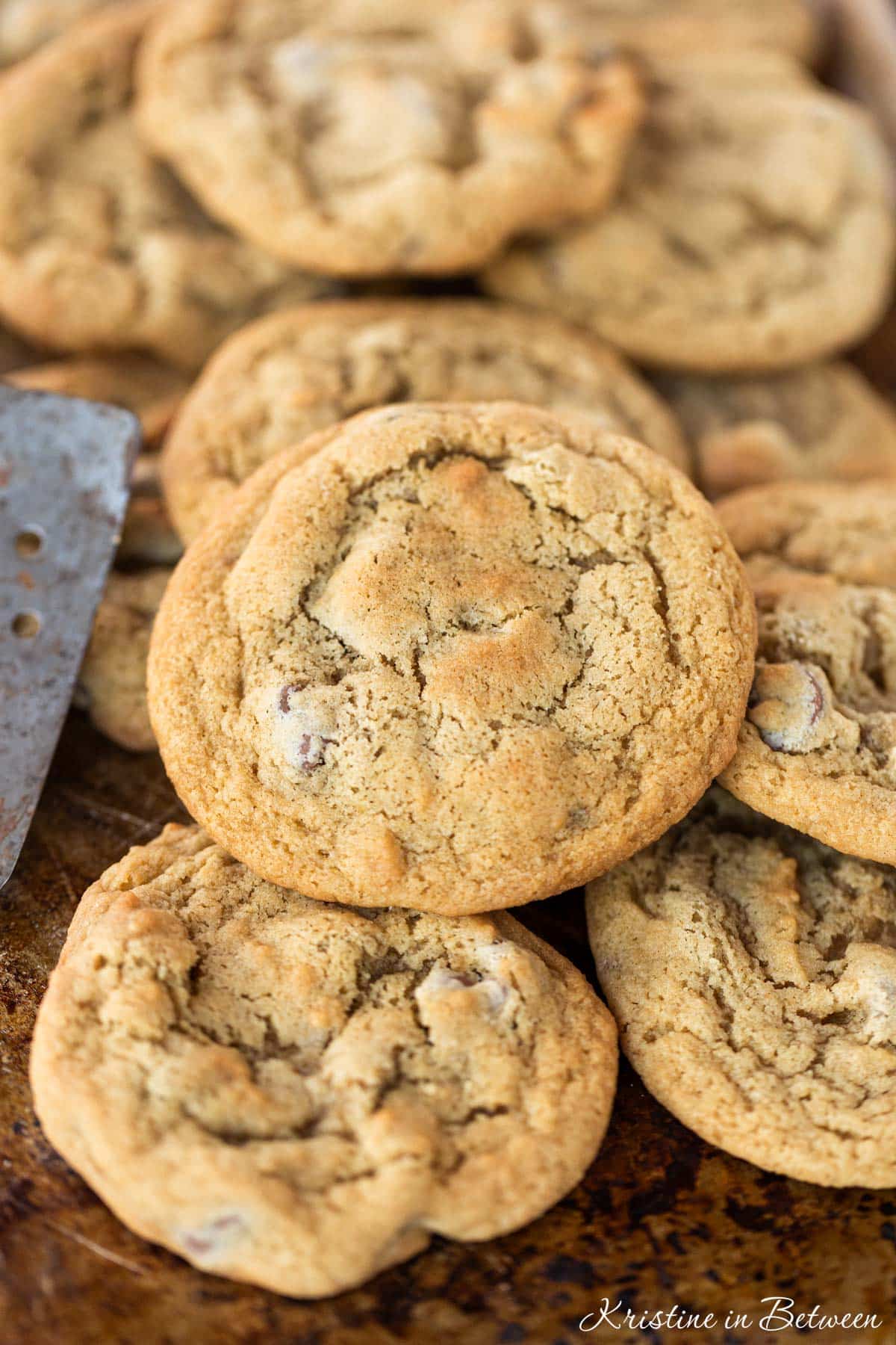 A bunch of cookies laying on an old baking sheet with a spatula.