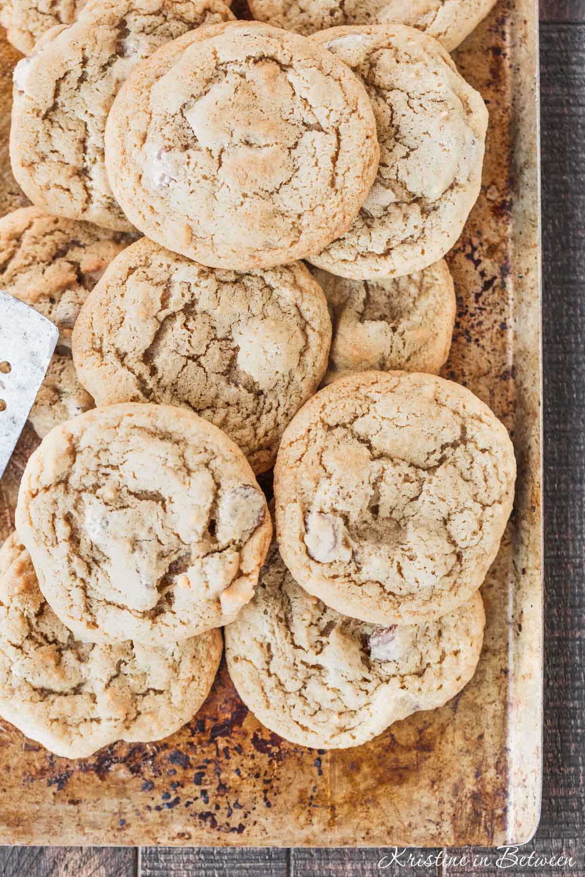 A bunch of cookies laying on an old baking sheet with a spatula.