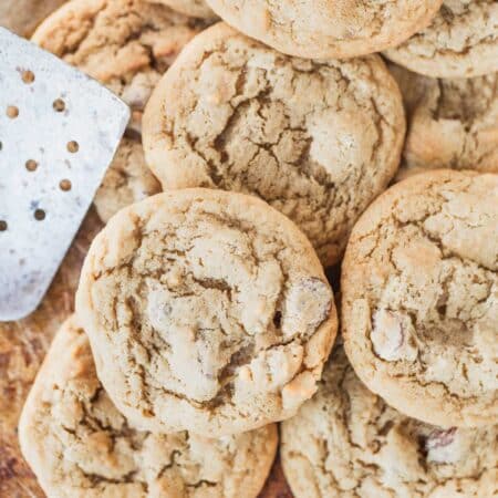A bunch of cookies laying on an old baking sheet with a spatula.