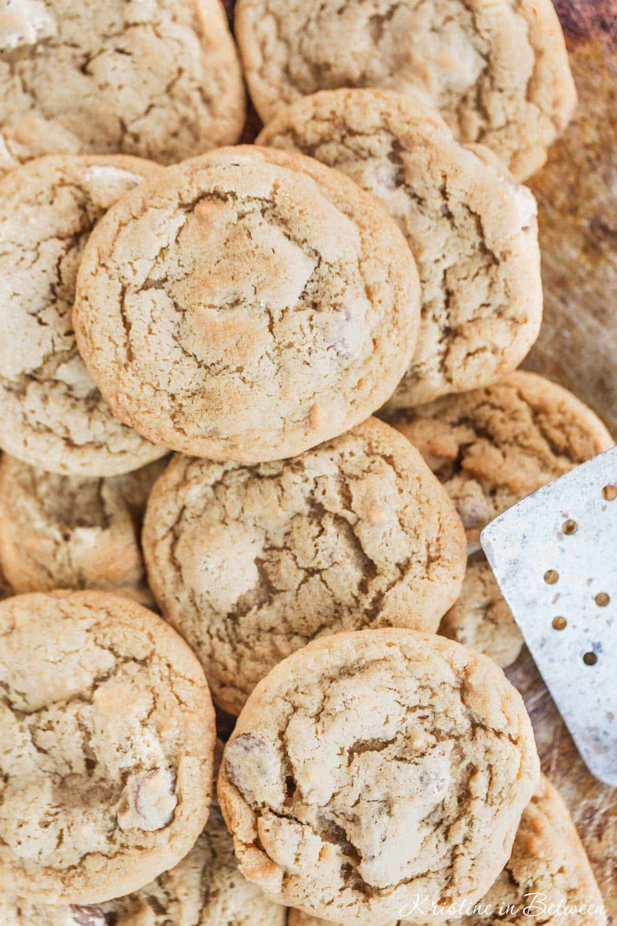 A bunch of cookies laying on an old baking sheet with a spatula.