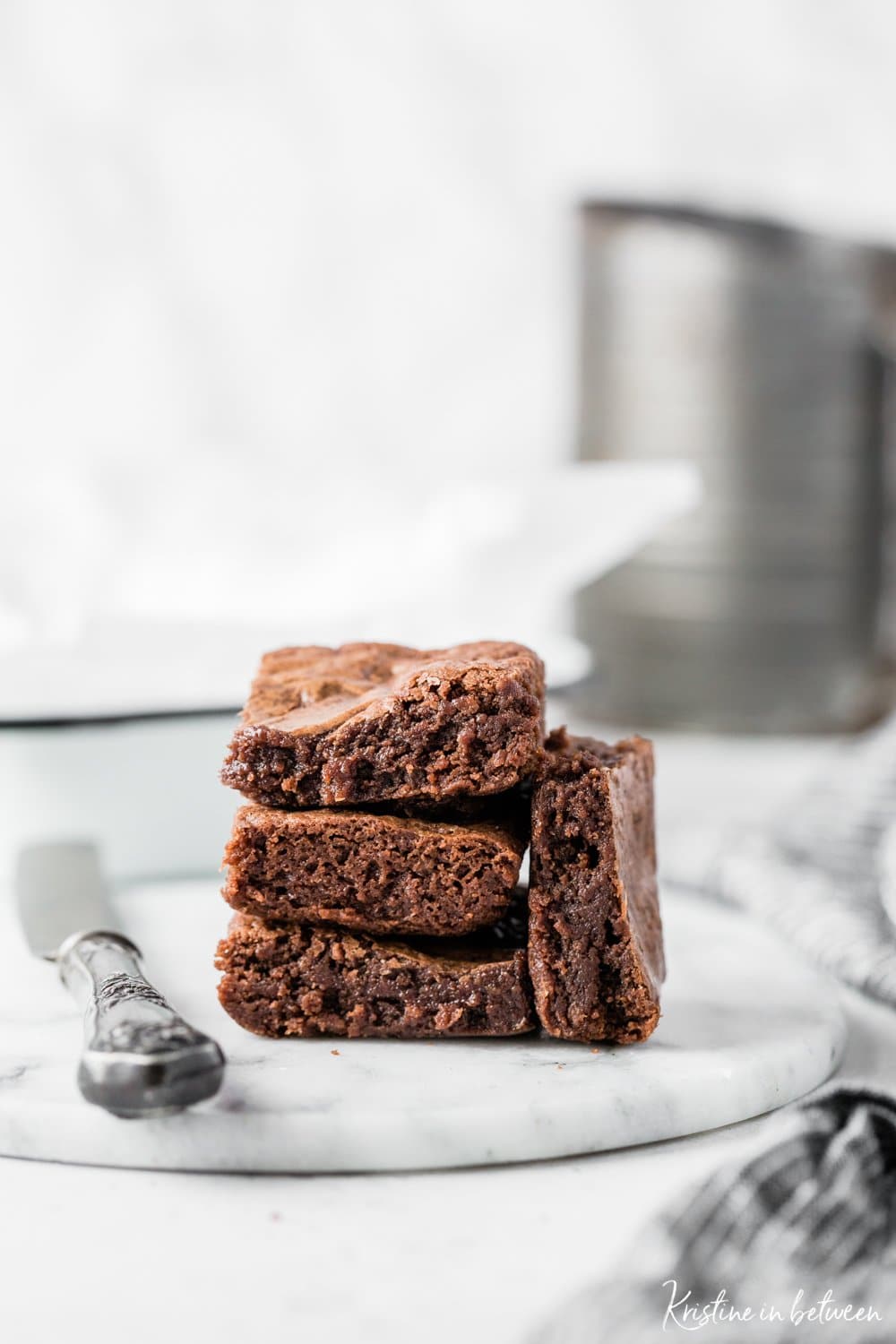 Brownies stacked up on a marble plate with a knife and a striped napkin.