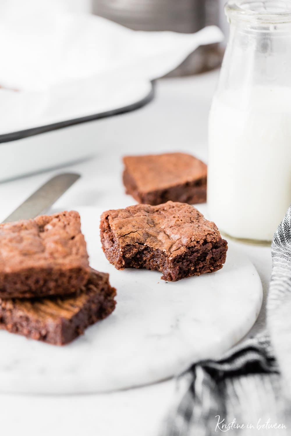 A few brownies sitting on a marble plate, one with a bite out of it.