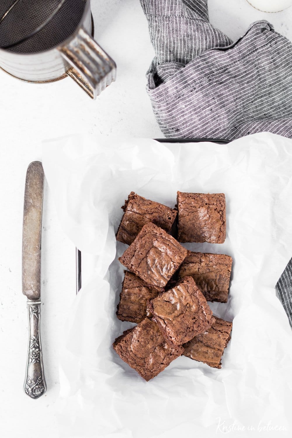 Cut up brownies sitting in a metal bowl with an antique knife next to them.