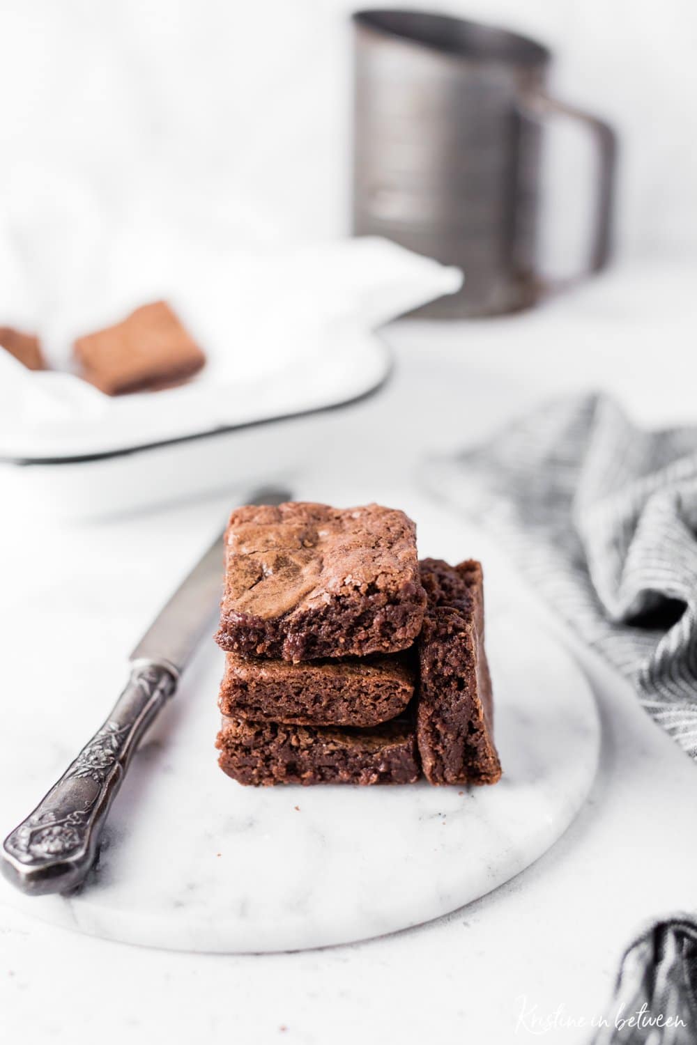 A stack of brownies sitting on a marble plate with an antique knife and a striped napkin.