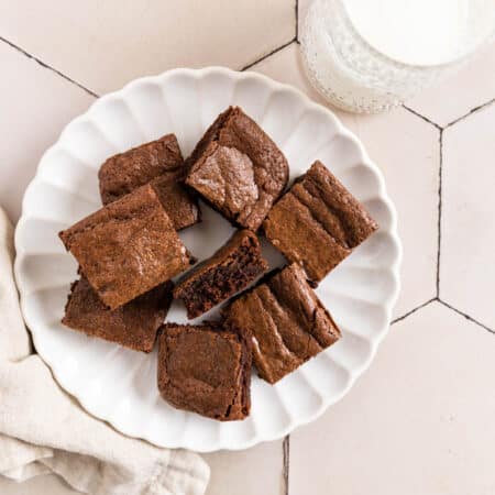 Brownies cut in squares on a white plate with a glass of milk next to it.