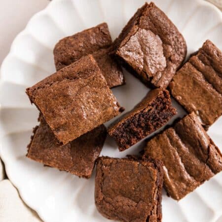 Brownies cut in squares on a white plate with a glass of milk next to it.