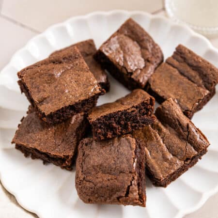 Brownies cut in squares on a white plate with a glass of milk next to it.