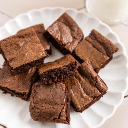 Brownies cut in squares on a white plate with a glass of milk next to it.