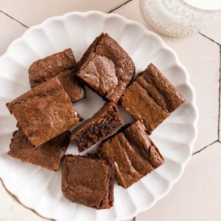 Brownies cut in squares on a white plate with a glass of milk next to it.