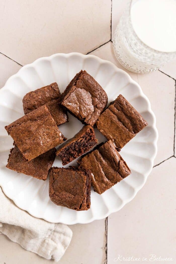 Brownies cut in squares on a white plate with a glass of milk next to it.