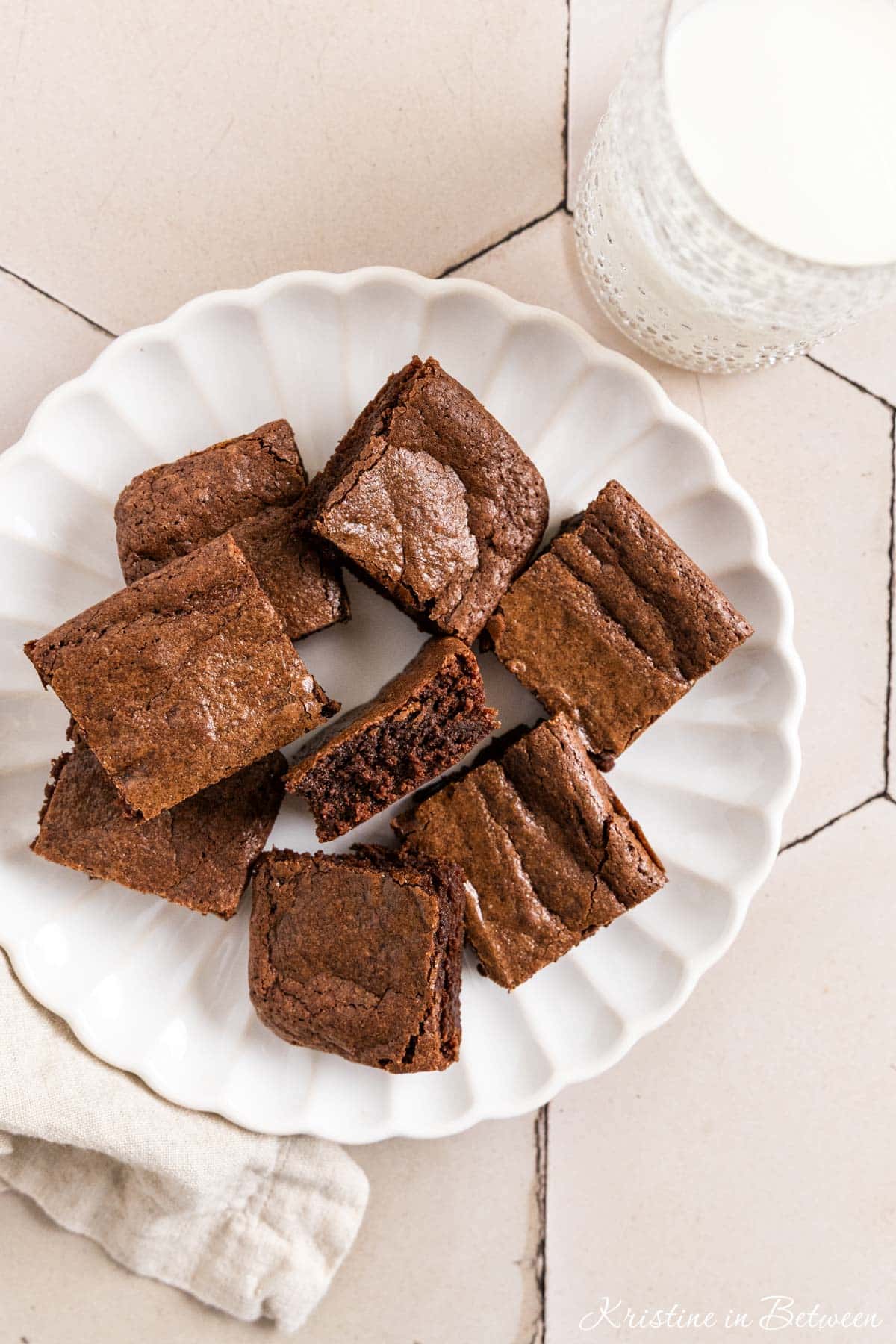 Brownies cut in squares on a white plate with a glass of milk next to it.