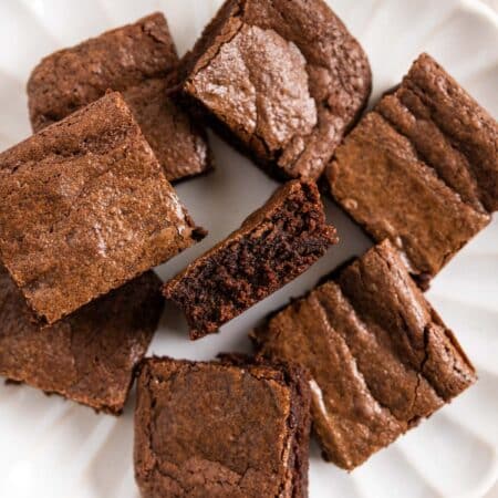 Brownies cut in squares on a white plate with a glass of milk next to it.