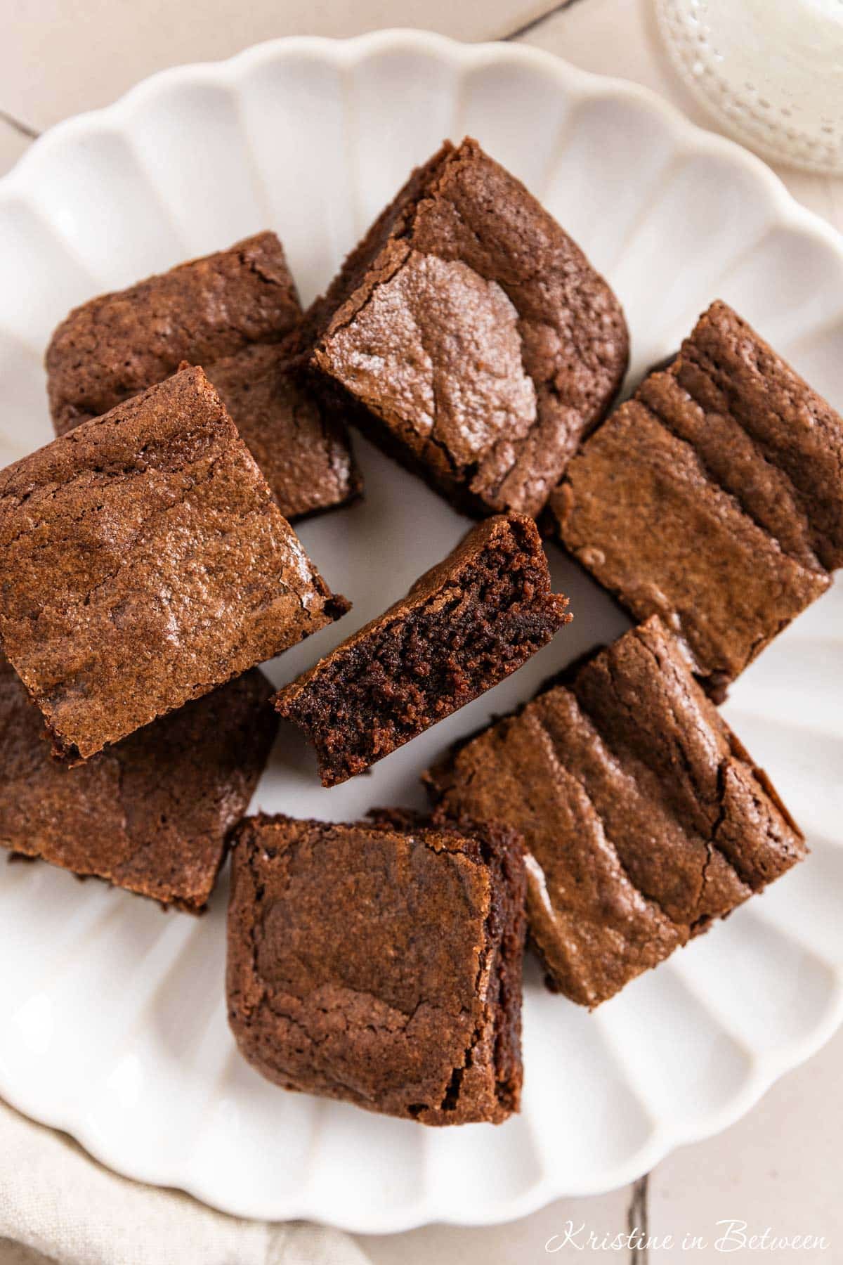 Brownies cut in squares on a white plate with a glass of milk next to it.