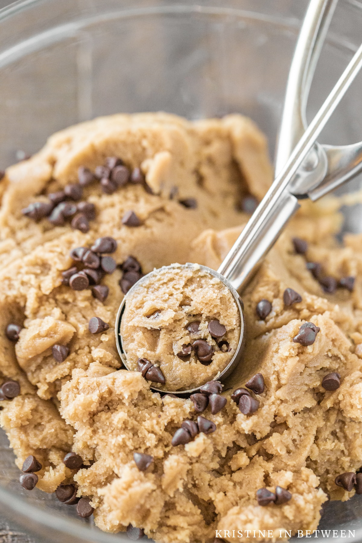 A scoop of basic cookie dough with chocolate chips in a bowl with a cookie scoop.