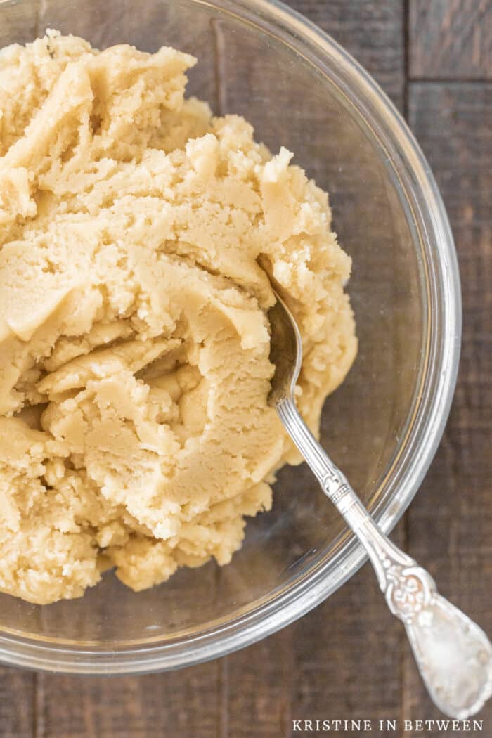 A bowl of basic sugar cookie dough with a spoon in it.