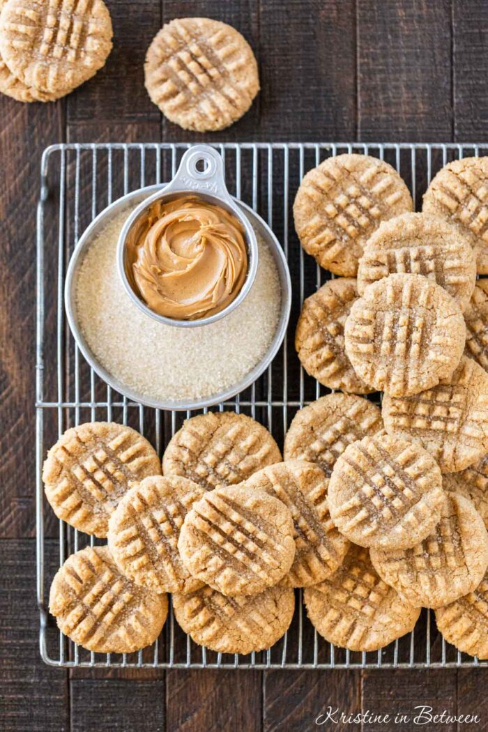 3 ingredient peanut butter cookies laying on a wire cooling rack with a small cup of peanut butter next to them.