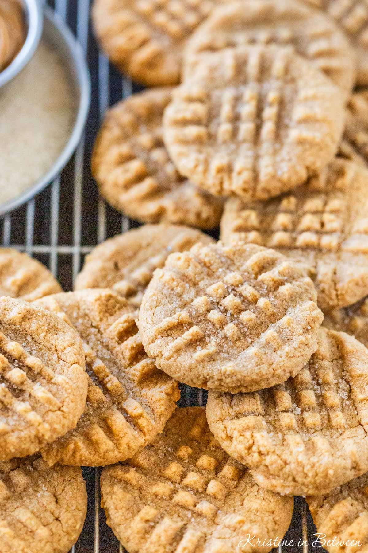 4 ingredient peanut butter cookies with vanilla laying on a wire cooling rack with a small cup of peanut butter next to them.