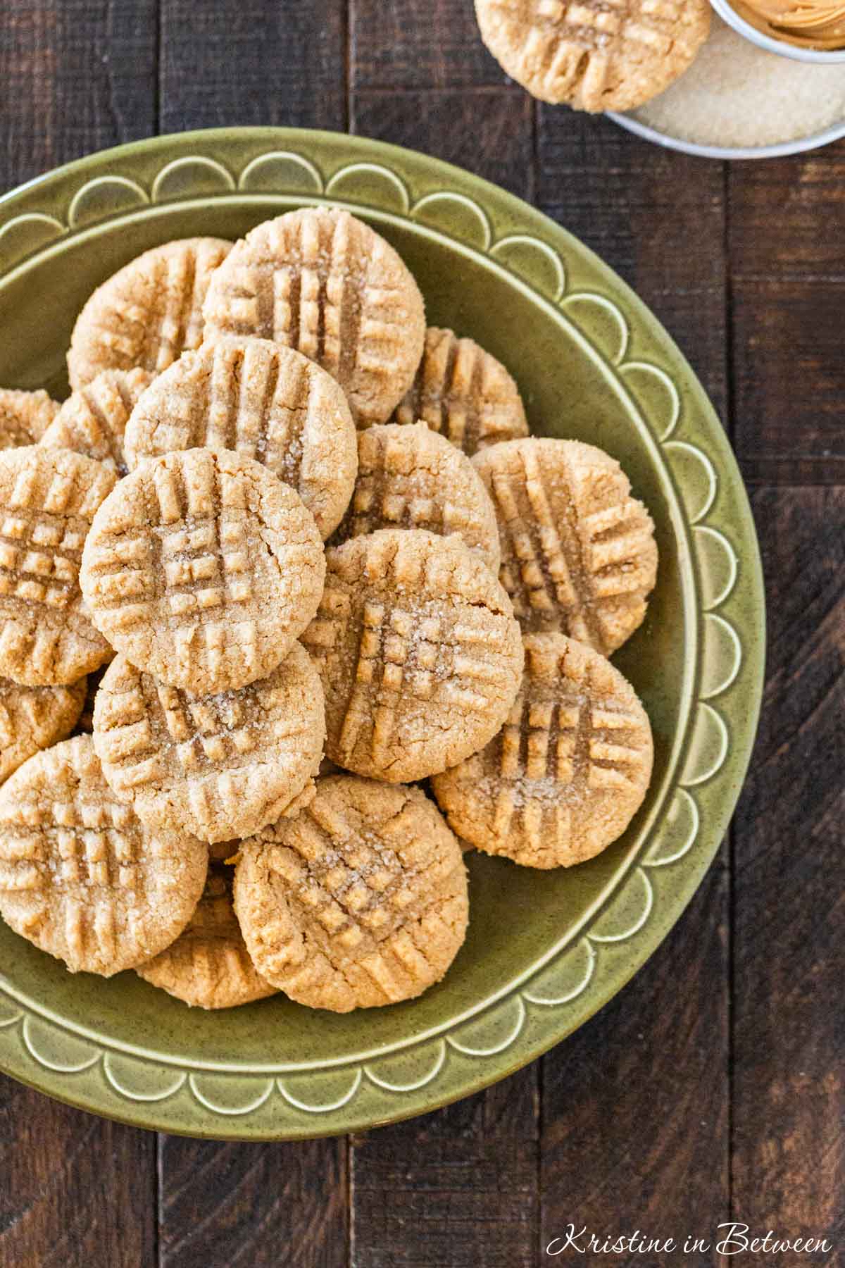 3 ingredient peanut butter cookies laying on a green plate with a small cup of peanut butter next to them.