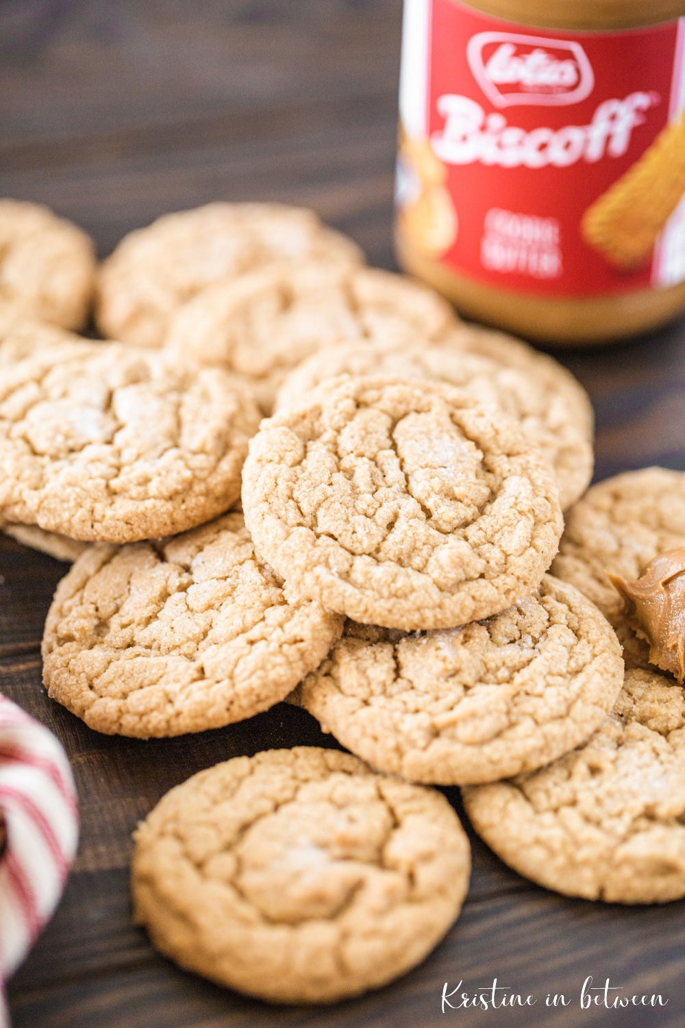 A stack of cookies laying on a wooden table with a jar of cookie butter in the background.