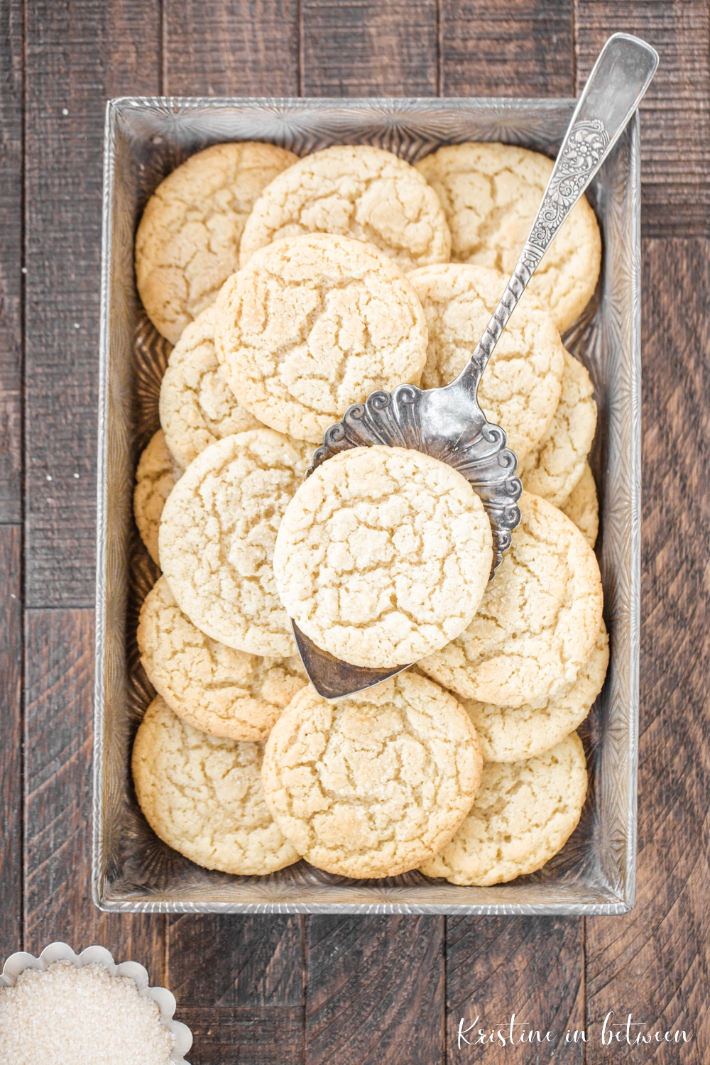 Cookies in a metal tin with one sitting on an antique spatula.