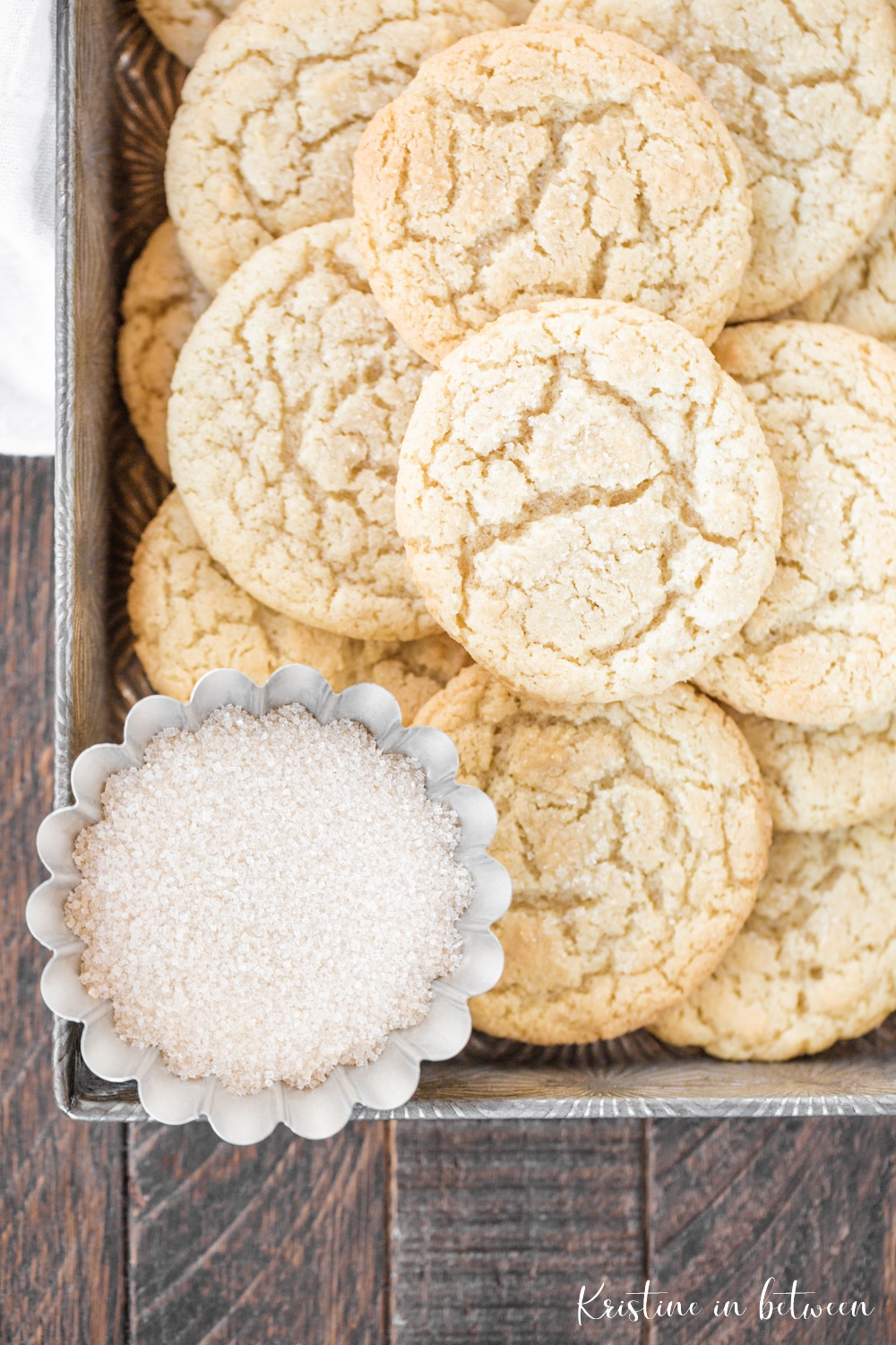 Cookies in a metal tin with a bowl of sugar sitting next to them.