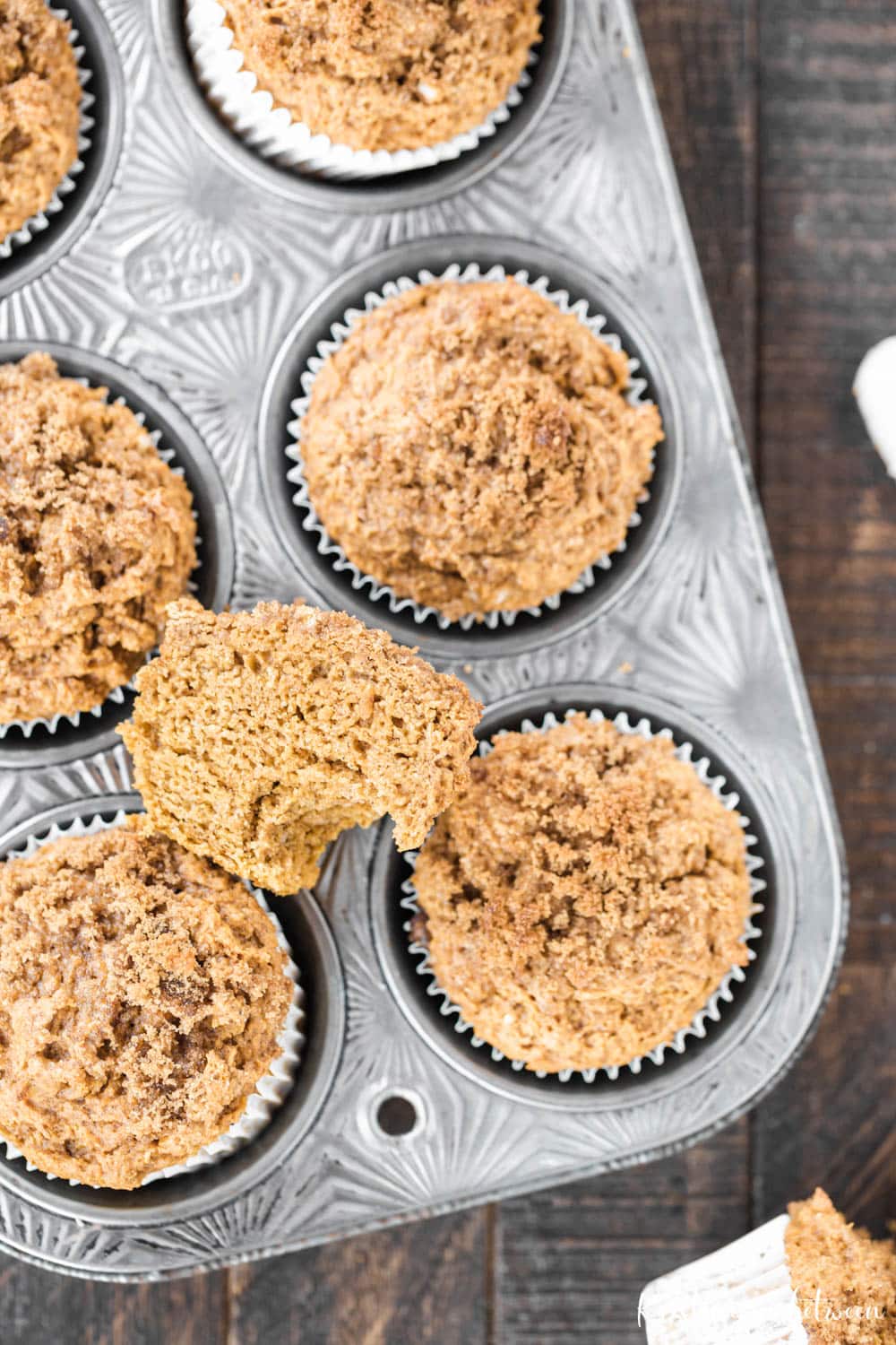 Pumpkin muffins sitting in a muffin tin with one cut in half and a bite out of it.