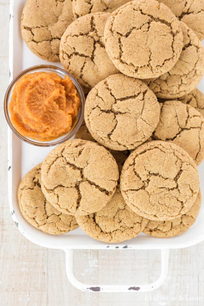 Cookies laying on a white tray with a small bowl of pumpkin puree.
