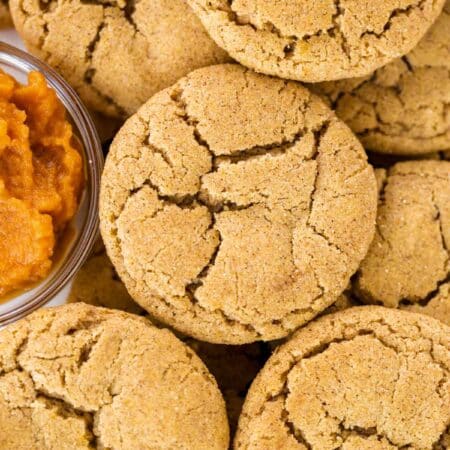 Pumpkin snickerdoodle cookies laying on a white tray with a small bowl of pumpkin puree next to them.
