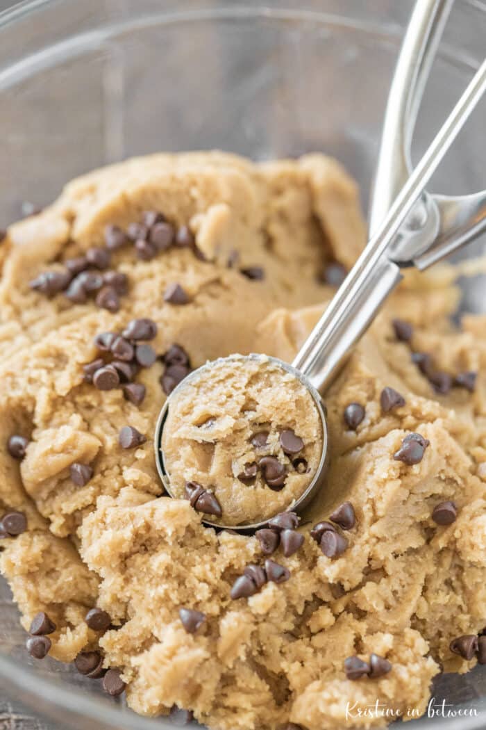 A bowl of cookie dough with chocolate chips and a scoop on top.