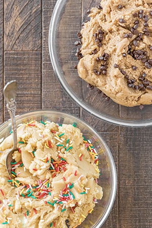Two bowls of cookie dough sitting on a. wooden table.