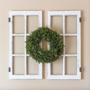 Wooden window frames hanging on a wall with a green wreath.
