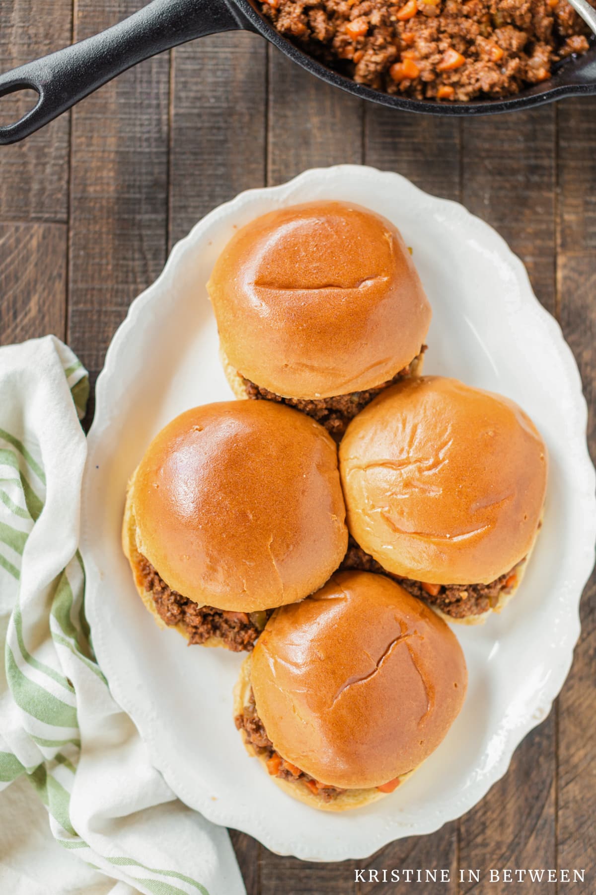 Sloppy Joes sitting on a white platter with a green napkin sitting next to them.
